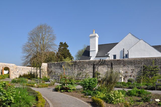 A stone wall, a garden path, and a building with a white facade and a chimney.