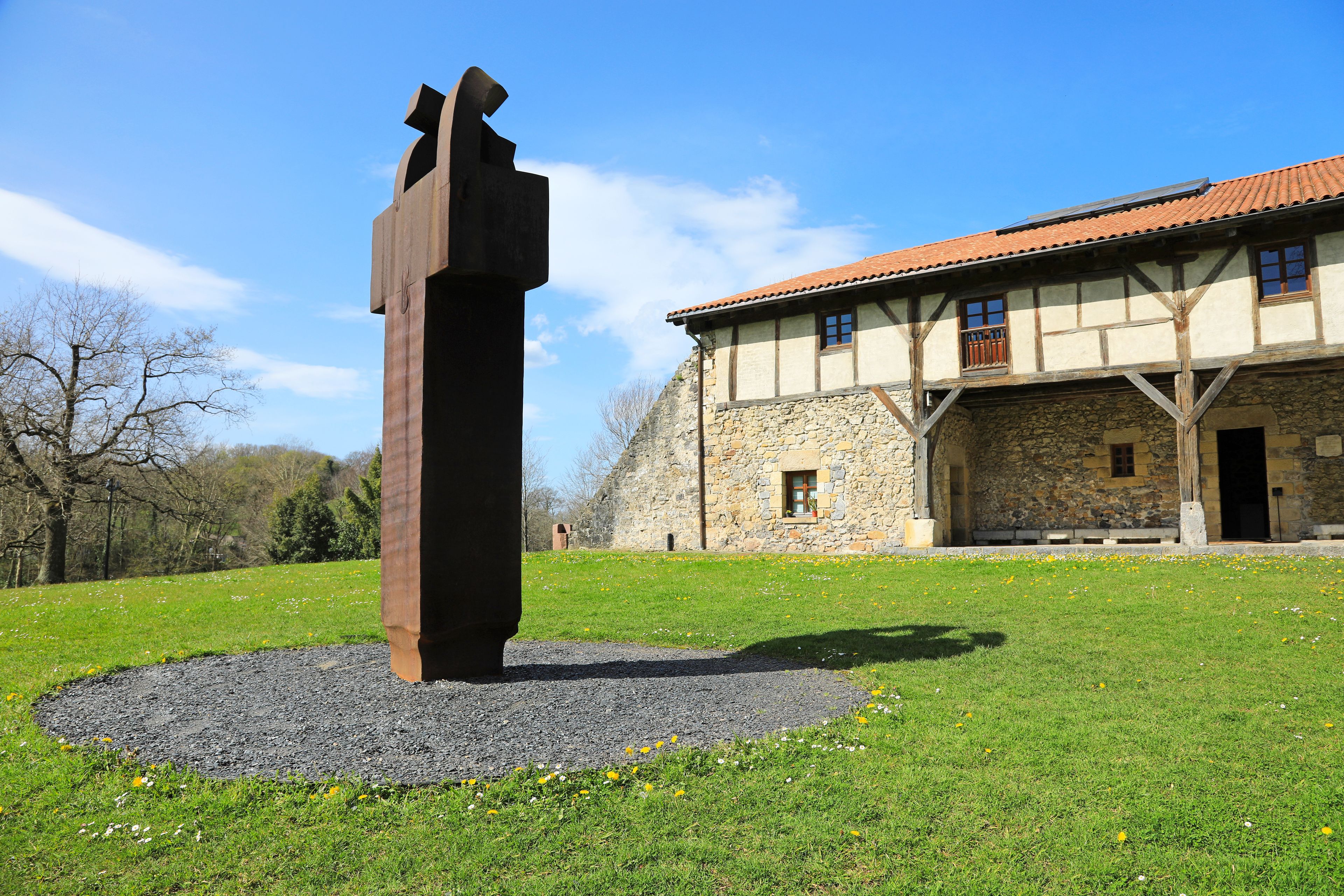 Una escultura en un área con césped, con un edificio de piedra al fondo.