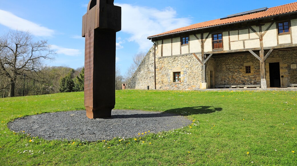 Una escultura en un área con césped, con un edificio de piedra al fondo.