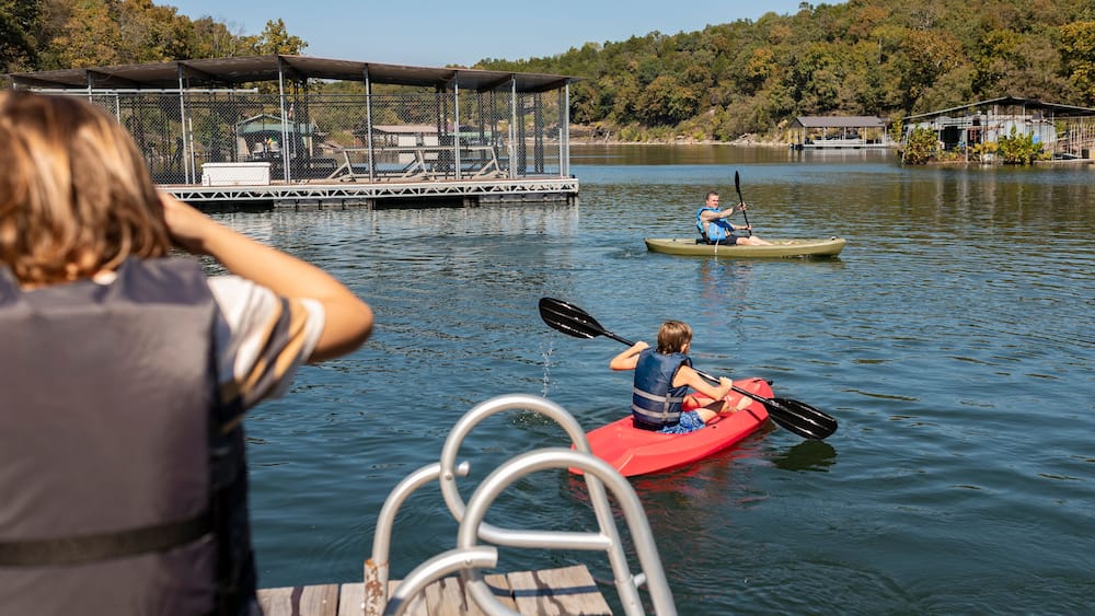 boy watching brother and dad kayak on lake