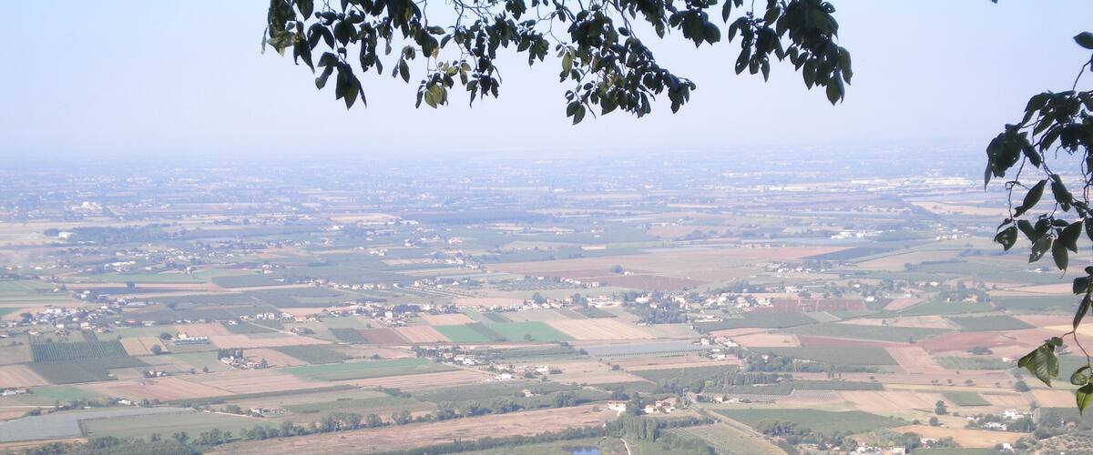 A panoramic view of a rural landscape with fields, a castle, and a lake.