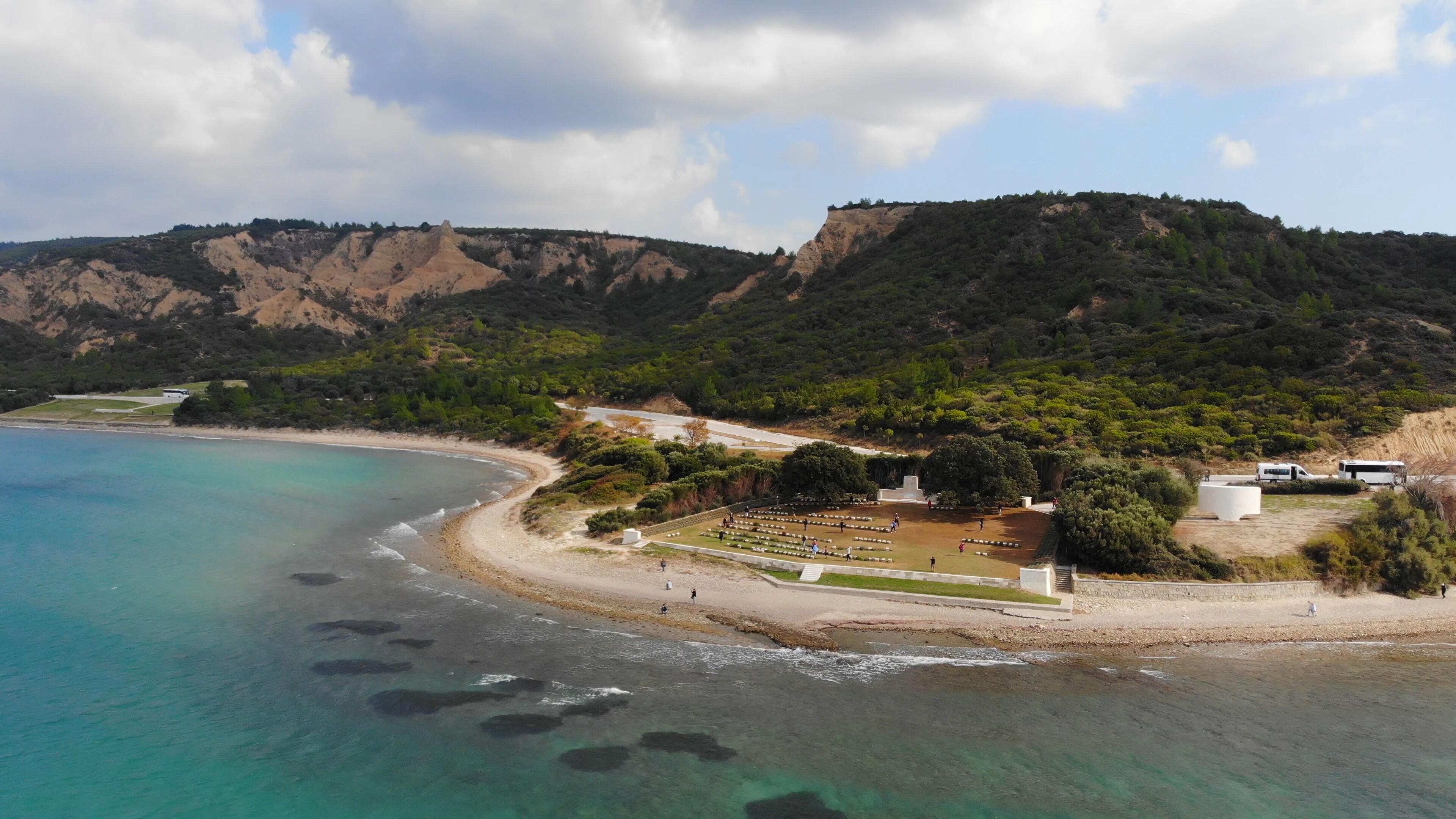 A coastal landscape with clear turquoise waters, a sandy beach, and a hilly backdrop.