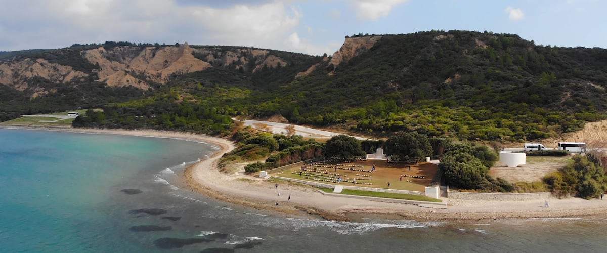 A coastal landscape with clear turquoise waters, a sandy beach, and a hilly backdrop.
