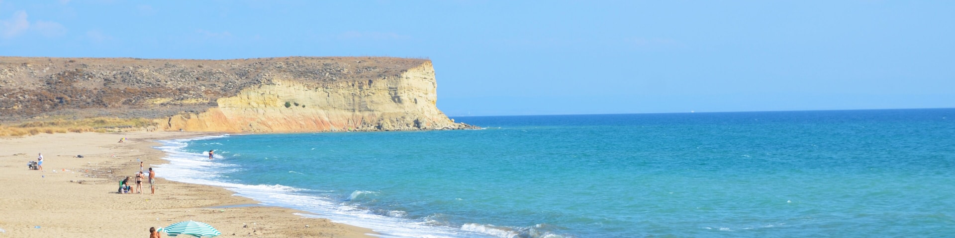 Una playa con gente tomando el sol, una orilla arenosa y un acantilado al fondo.