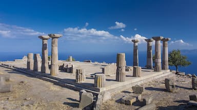 Ancient stone columns and ruins on a hillside with a clear blue sky.