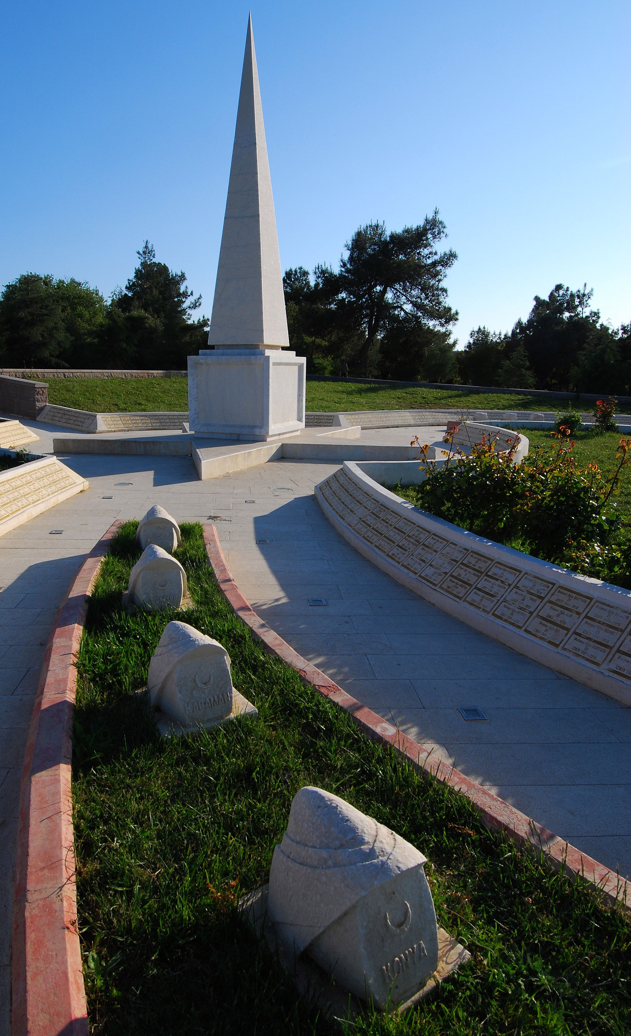 A monument with a pointed top, surrounded by a landscaped area with grass and a paved walkway.