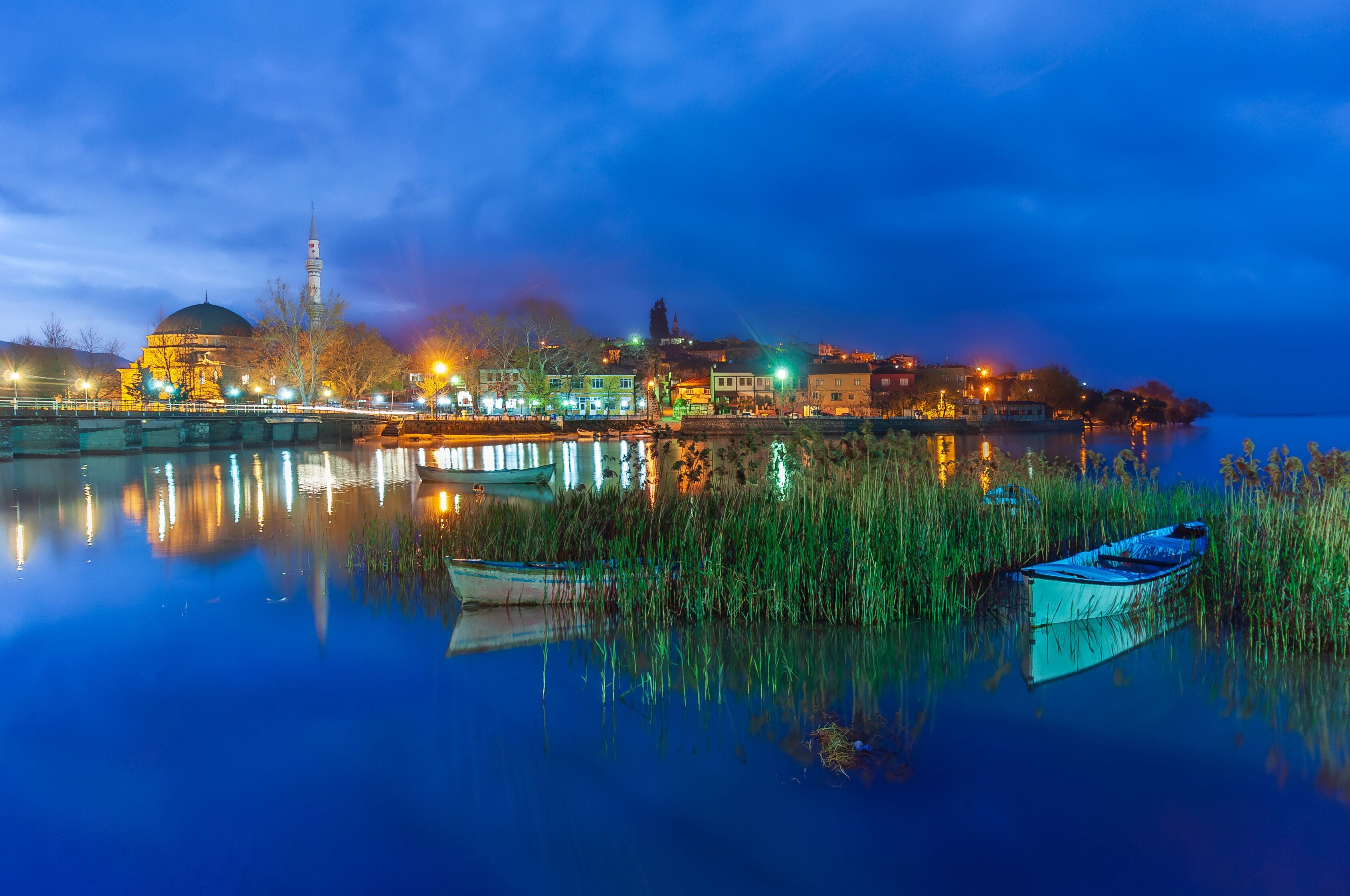 A calm river reflecting city lights, a prominent dome, and a tall minaret.