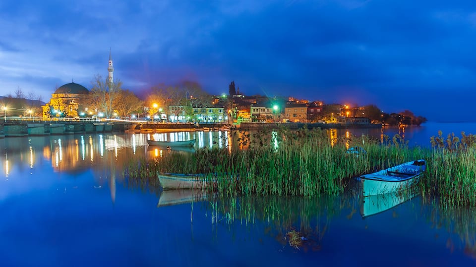 A calm river reflecting city lights, a prominent dome, and a tall minaret.