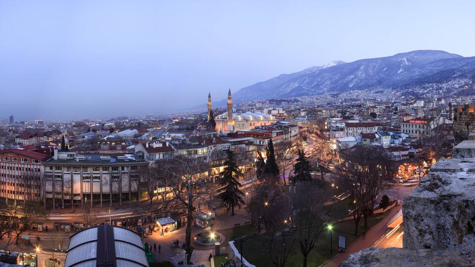 A cityscape with a prominent mosque, snow-covered buildings, and a mountain in the background.