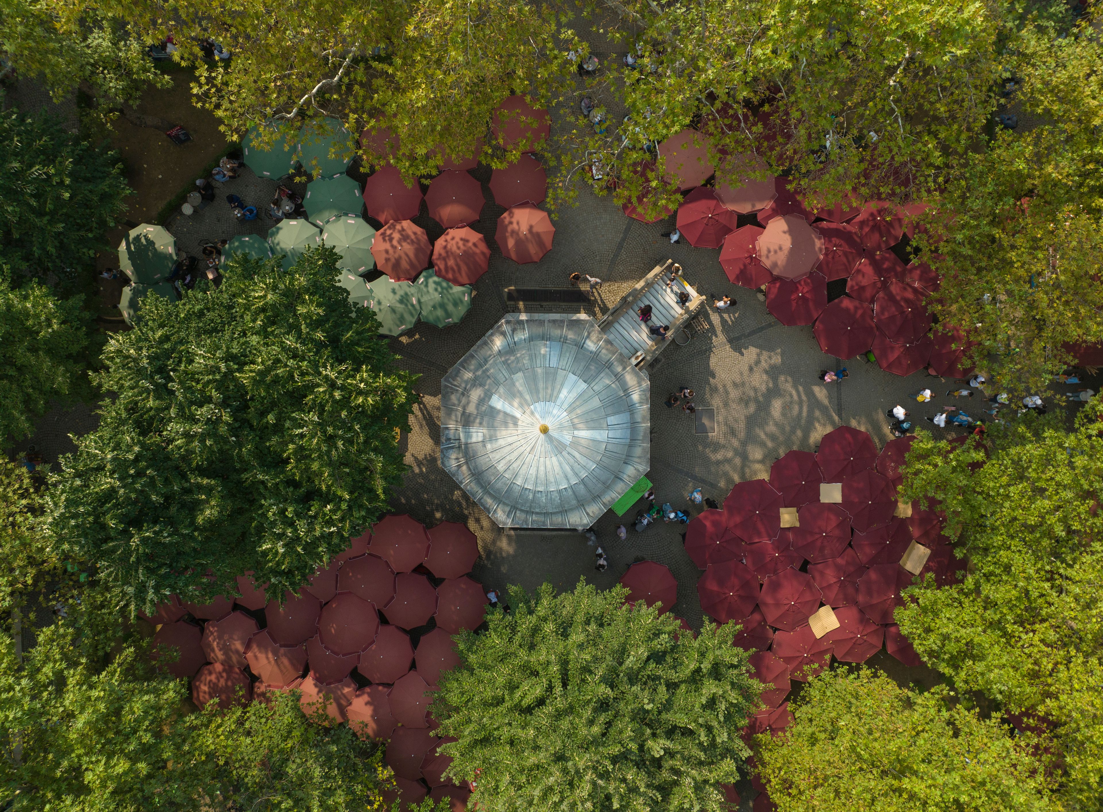An aerial view of a park with a central gazebo surrounded by trees and red umbrellas.