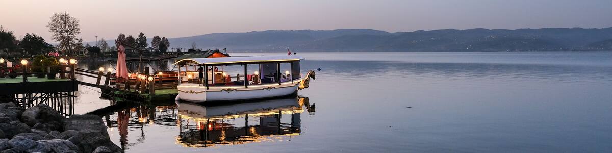 A calm lake with a boat docked at the pier, surrounded by rocks and a clear sky.
