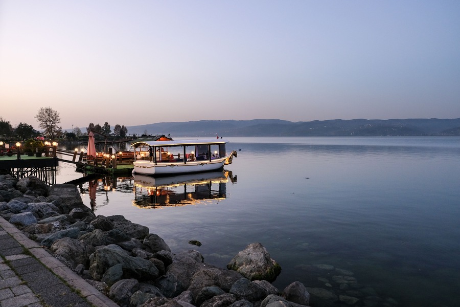 Ein ruhiger See mit einem Boot, das an der Anlegestelle liegt, umgeben von Felsen und einem klaren Himmel.