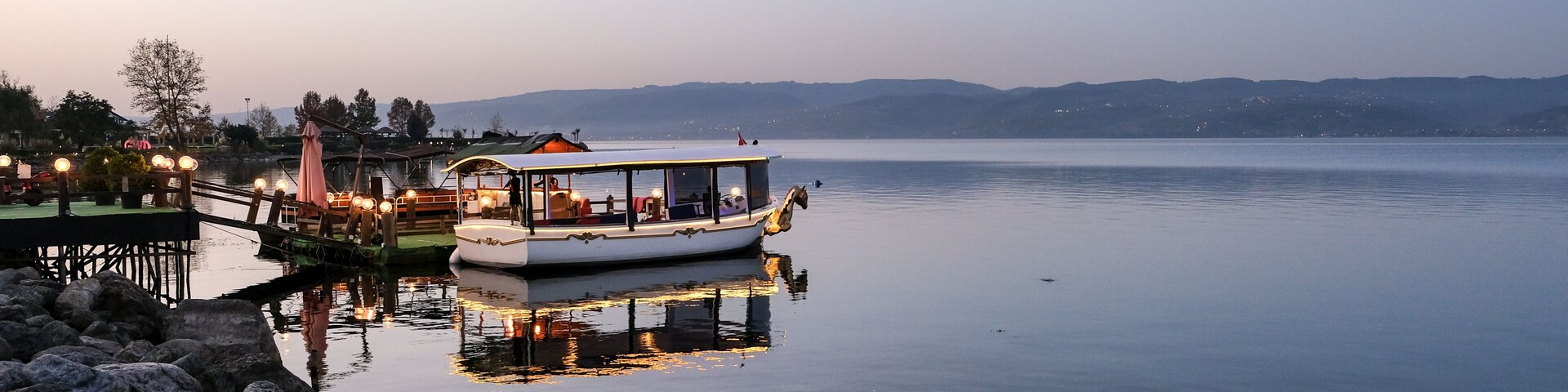 Un lac paisible, avec un bateau amarré au quai, entouré de rochers et surplombé d’un ciel dégagé.
