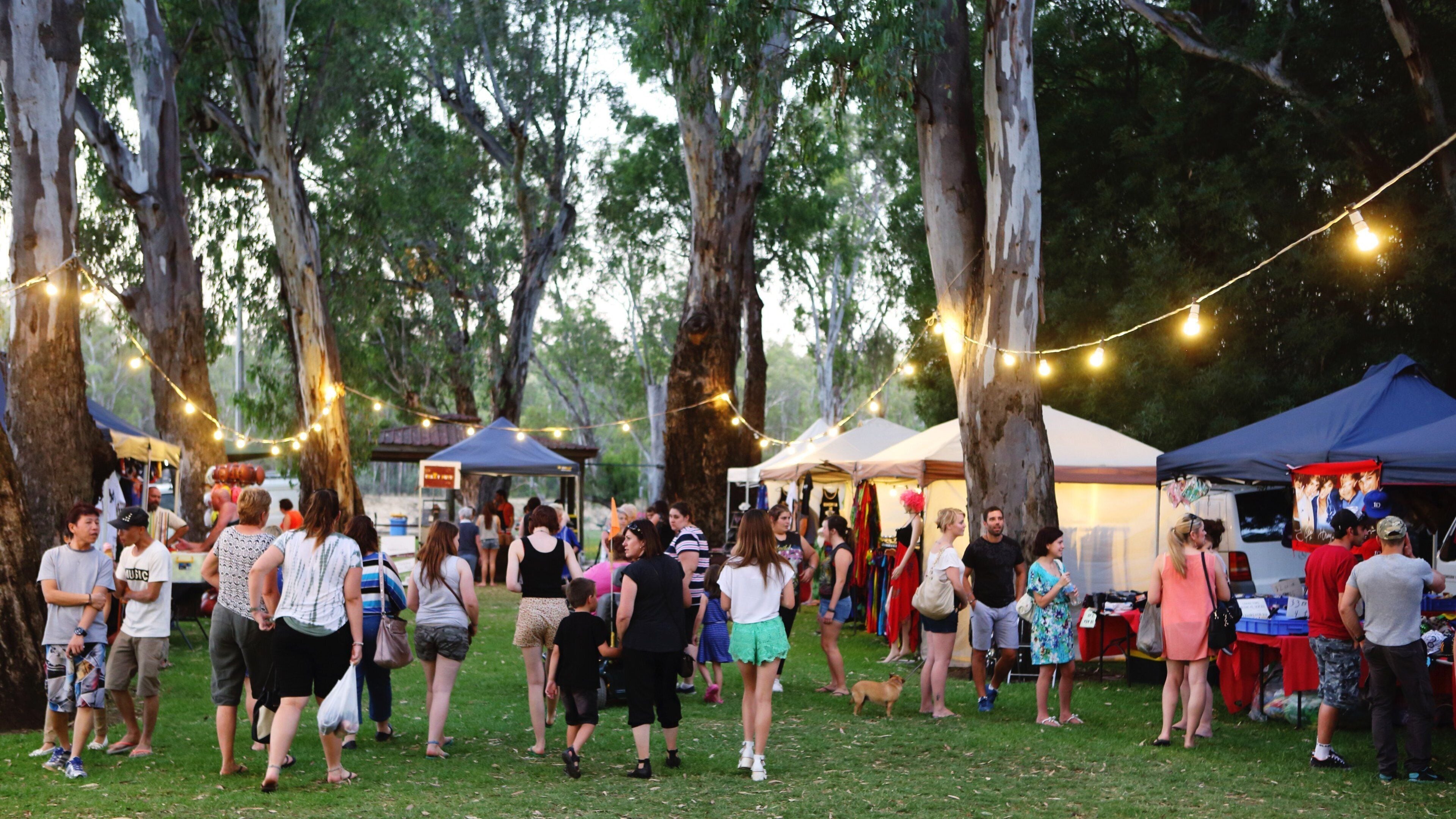 A group of people at an outdoor event with string lights and tents.