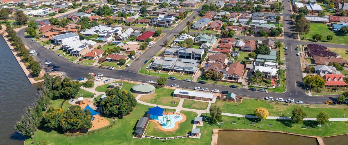 An aerial view of a residential area with houses, a park, and a body of water.
