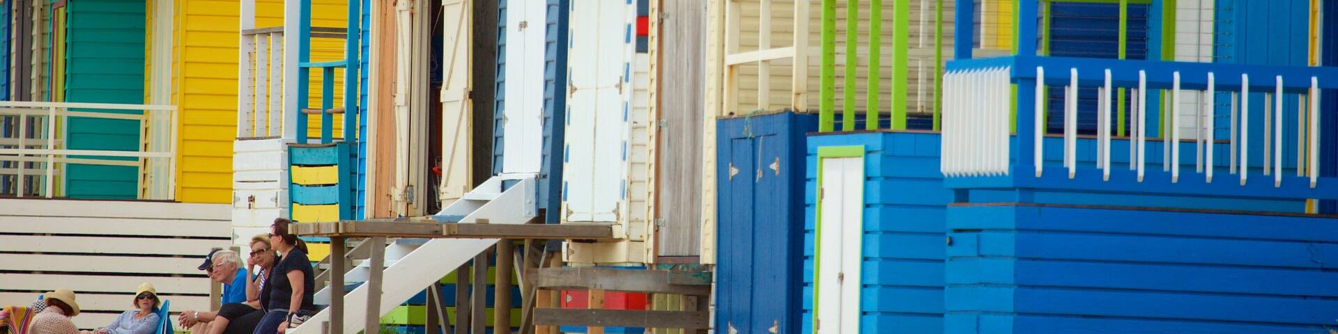 Colorful beach huts with a sandy beach and people sitting nearby.