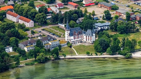 Ein Luftbild einer Stadt mit einem markanten, schlossartigen Gebäude, umgeben von Wohnhäusern und einem Fluss.