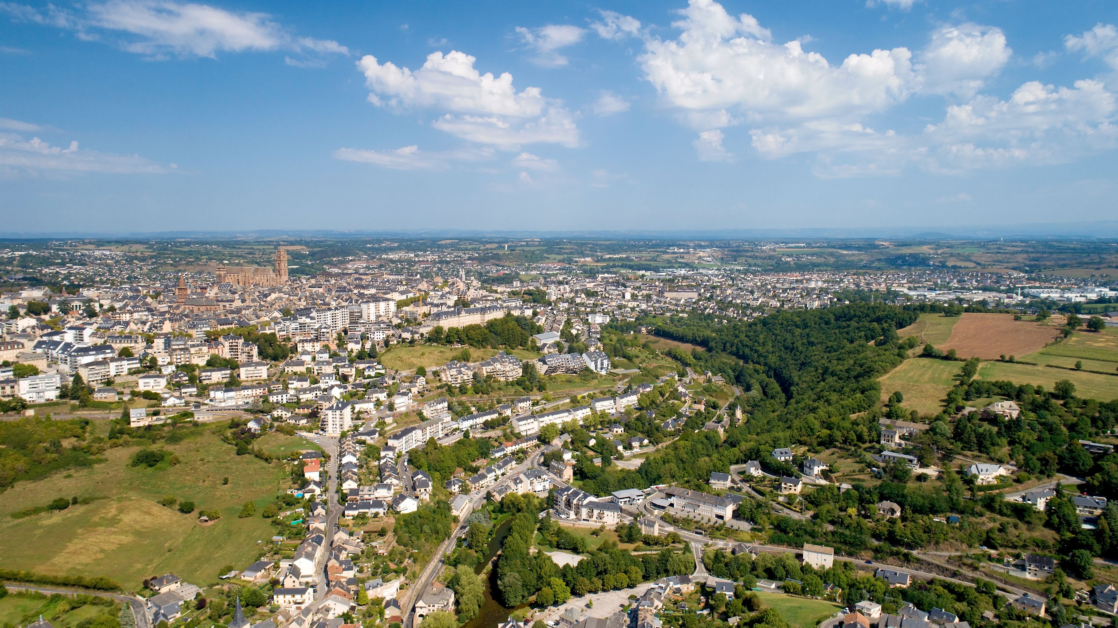 Une vue aérienne d’une ville avec un clocher d’église imposant, des quartiers résidentiels et des espaces verts.