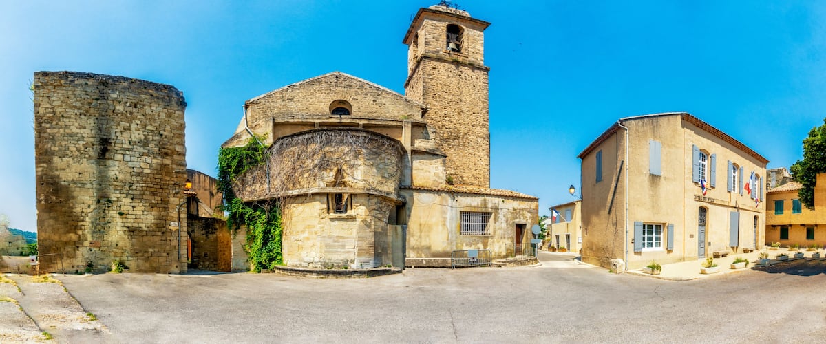 A historic town square with a prominent church featuring a bell tower, a stone wall, and a building labeled "Hotel de Ville".