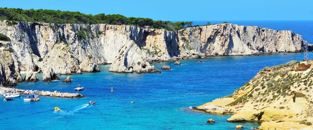A coastal landscape with cliffs, clear blue water, and boats.