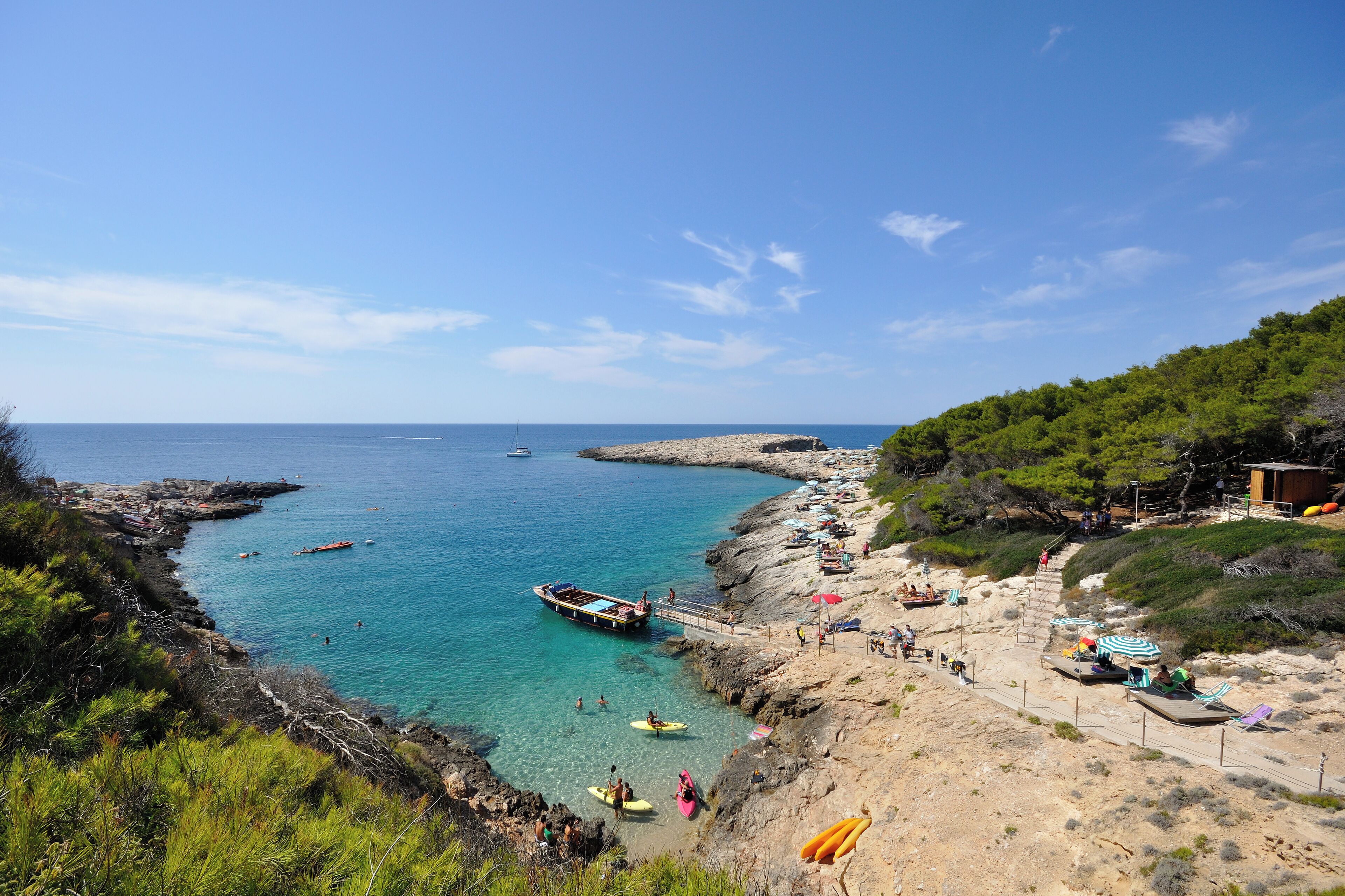 Zona costera con aguas turquesas cristalinas, costas rocosas y un muelle con barcos.