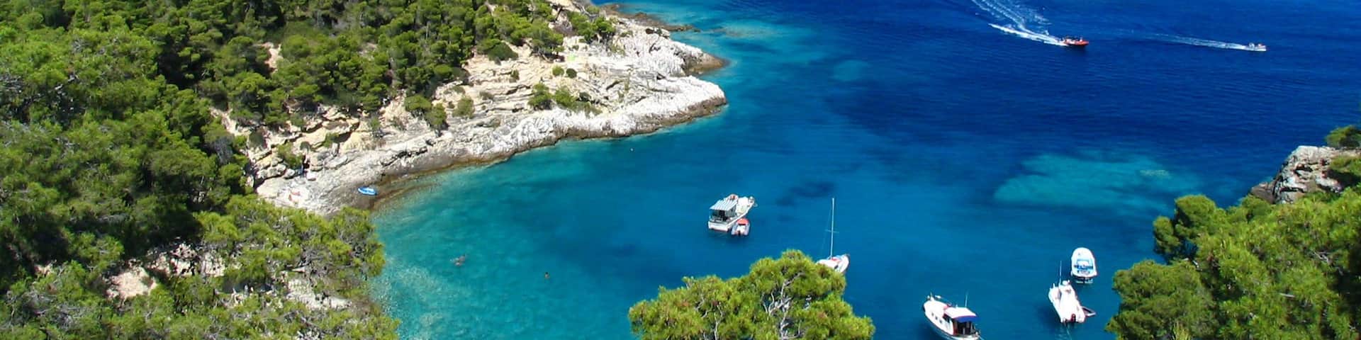 A coastal town with clear turquoise waters, boats, and a prominent rocky island with buildings.