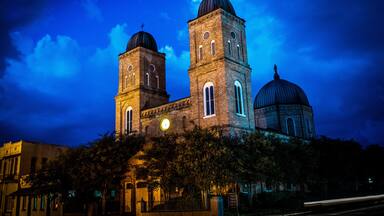 A historic church with two towers and a dome, surrounded by trees and under a twilight sky.