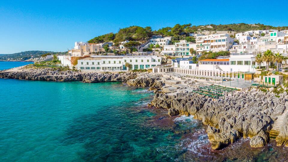 A coastal town with white buildings, rocky cliffs, and clear turquoise sea.