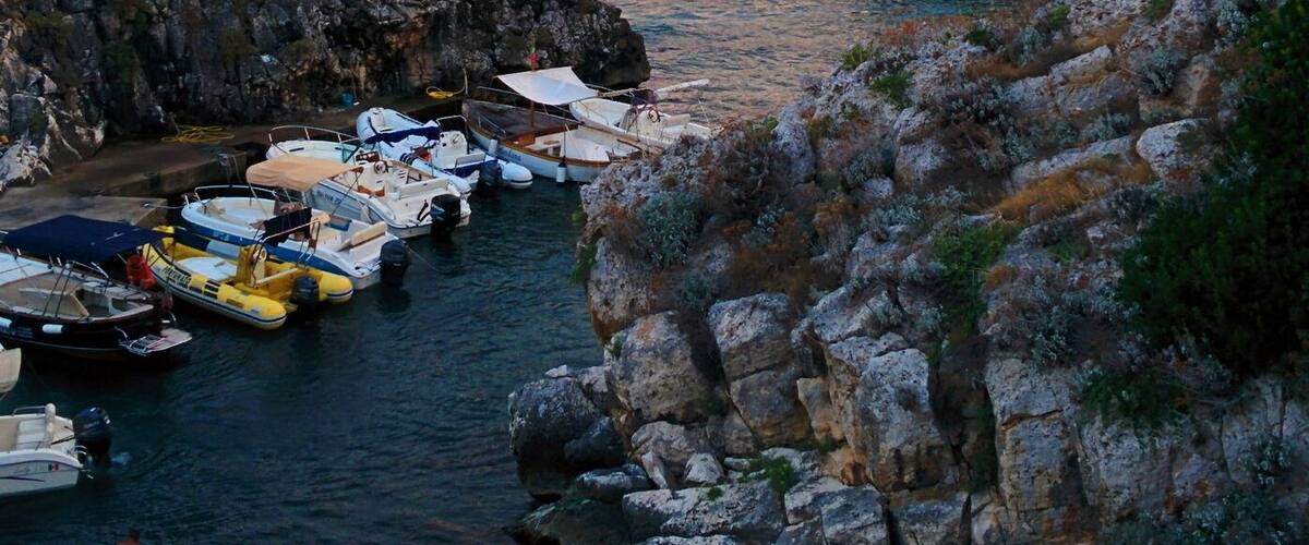 A coastal town with rocky cliffs, boats docked at a harbor, and buildings along the shoreline.