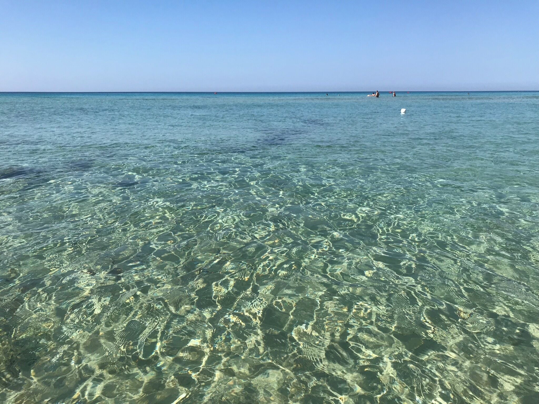 Clear shallow waters with visible underwater patterns and a distant boat on the horizon.