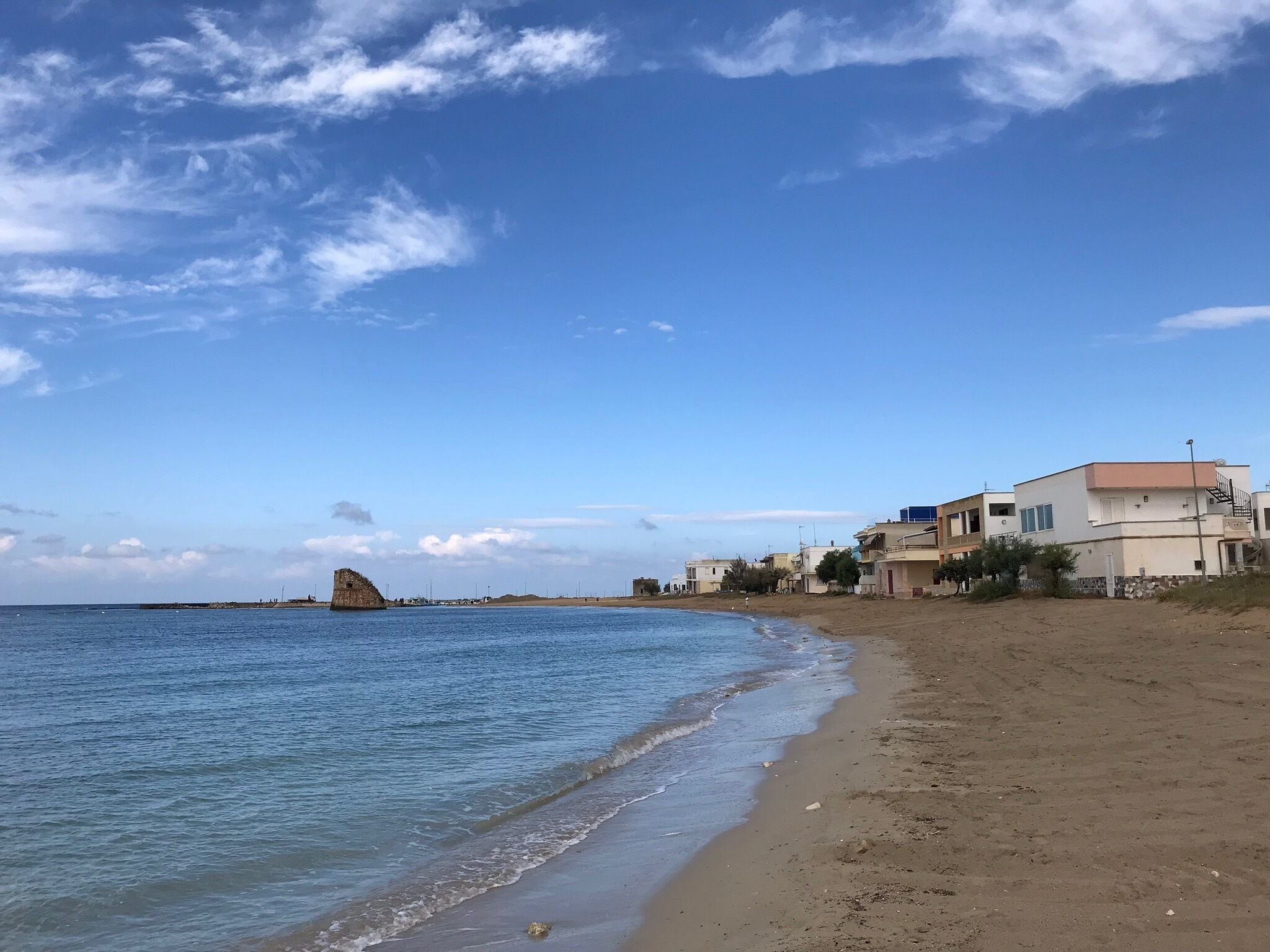 A beach with a rocky outcrop in the water, sandy shore, and residential buildings.