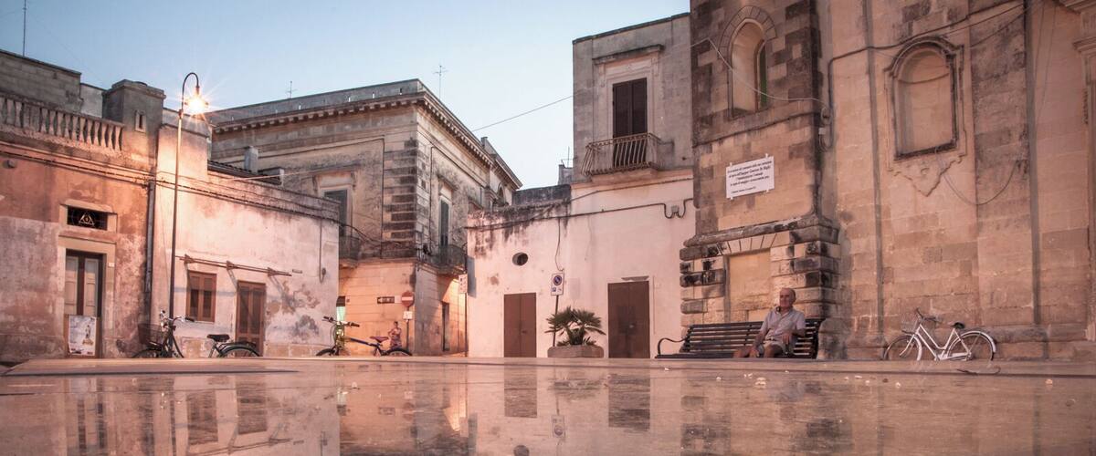 A historic square with a reflective water surface, old buildings, and a bicycle.