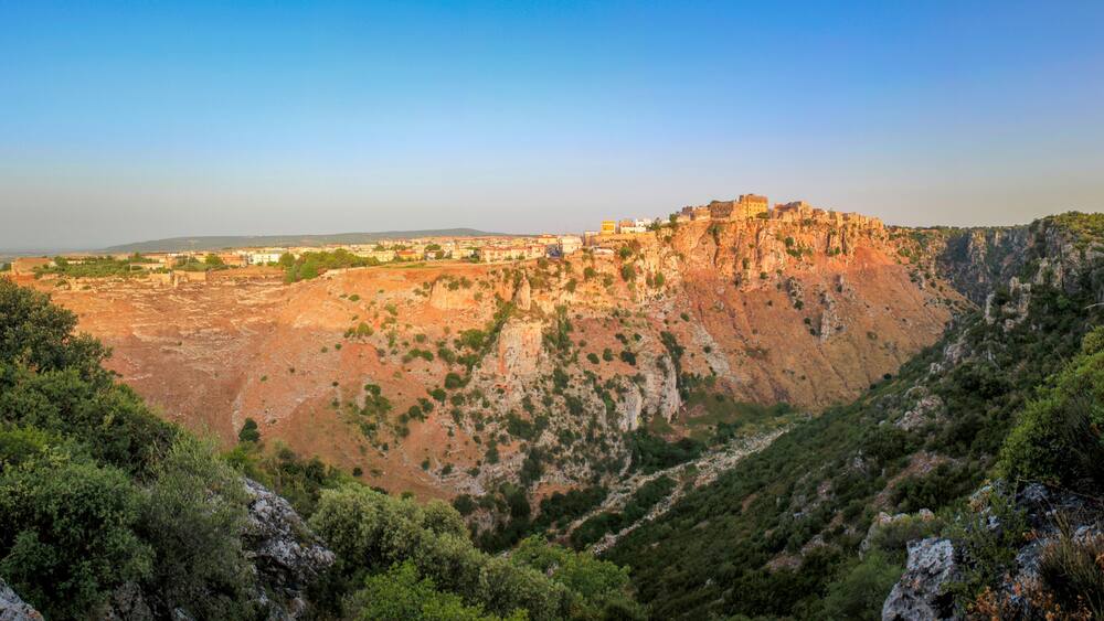 Ein zerklüfteter Berg mit einer befestigten Struktur auf der Spitze, umgeben von dichtem Grün und felsigem Gelände.