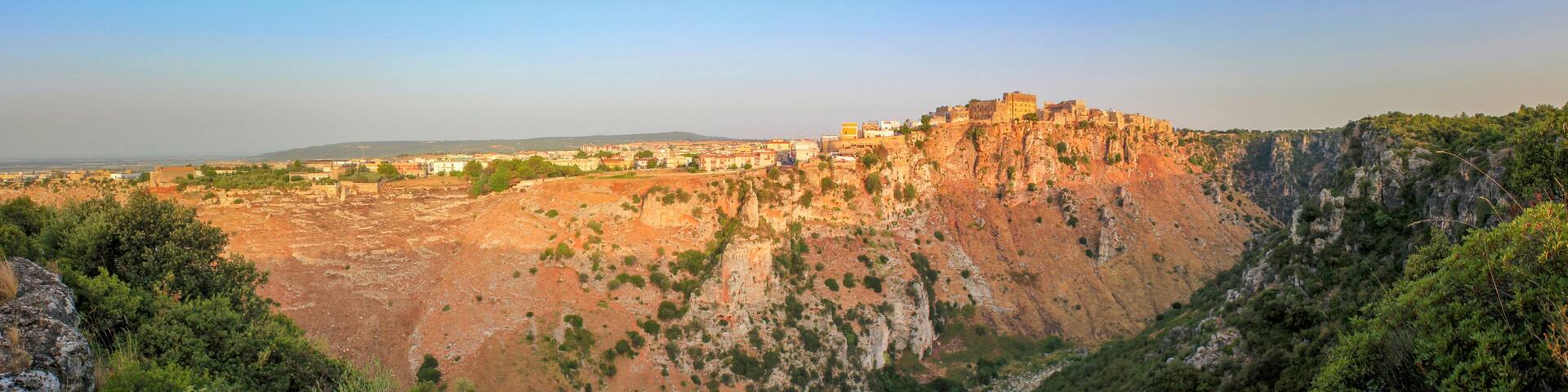 A rugged mountain with a fortified structure on top, surrounded by dense greenery and rocky terrain.