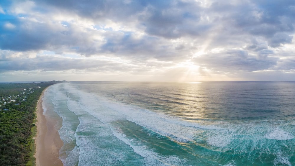 A coastal landscape with a beach, ocean waves, and a cloudy sky.