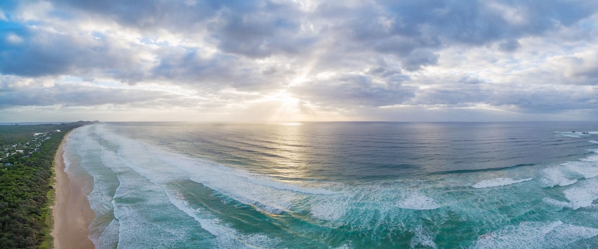 A coastal landscape with a beach, ocean waves, and a cloudy sky.