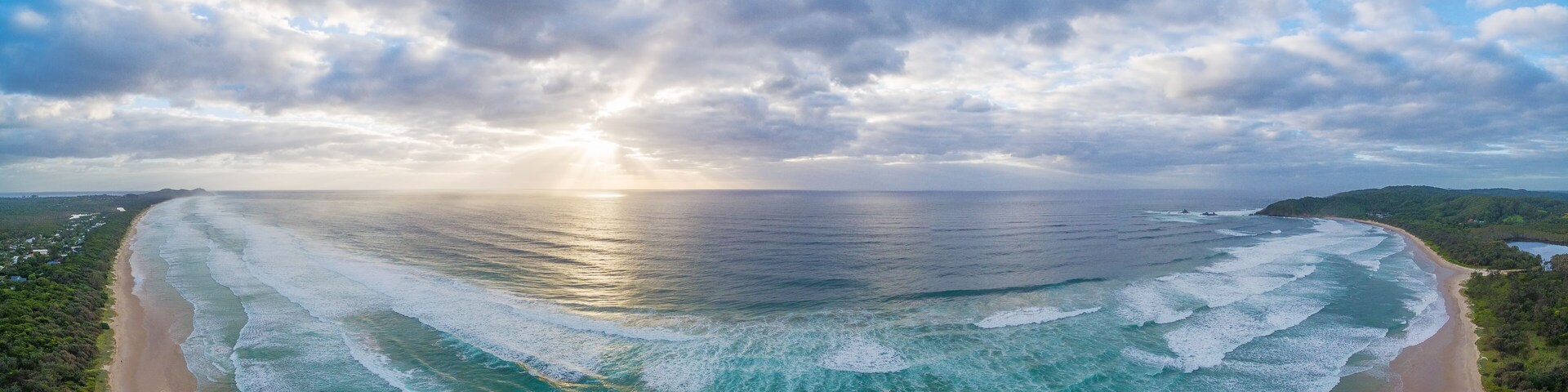 Un paisaje costero con playa, olas del océano y cielo nublado.