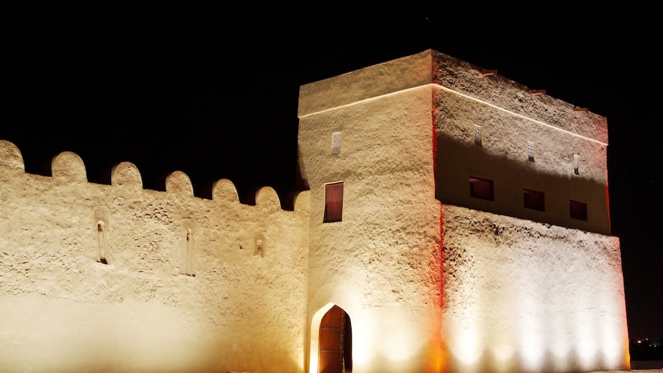 A medieval stone fortress with a tall tower, arched entrance, and crenellated walls at night.