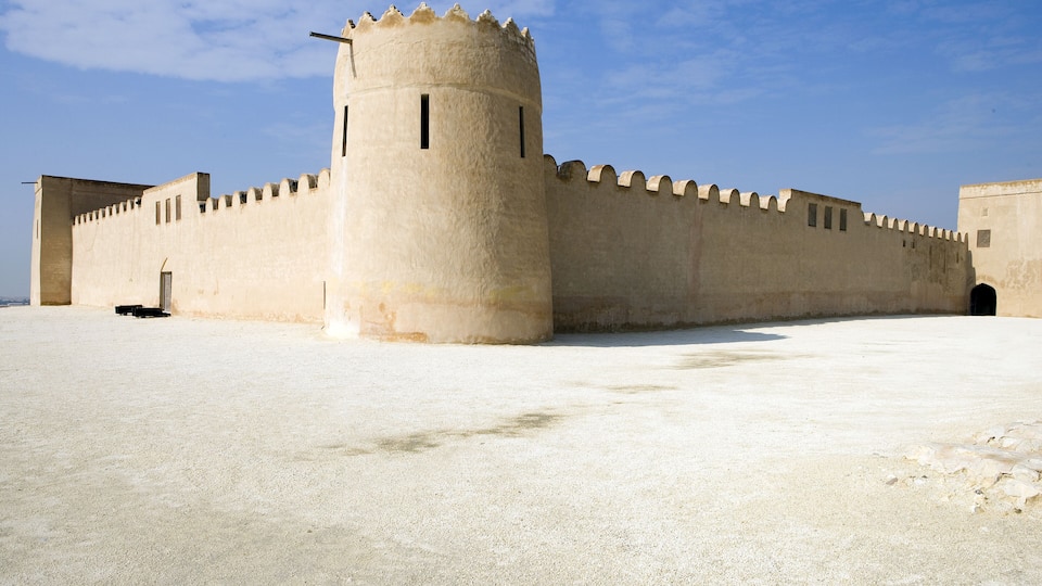 A large, beige fortress with a round tower and crenellated walls.