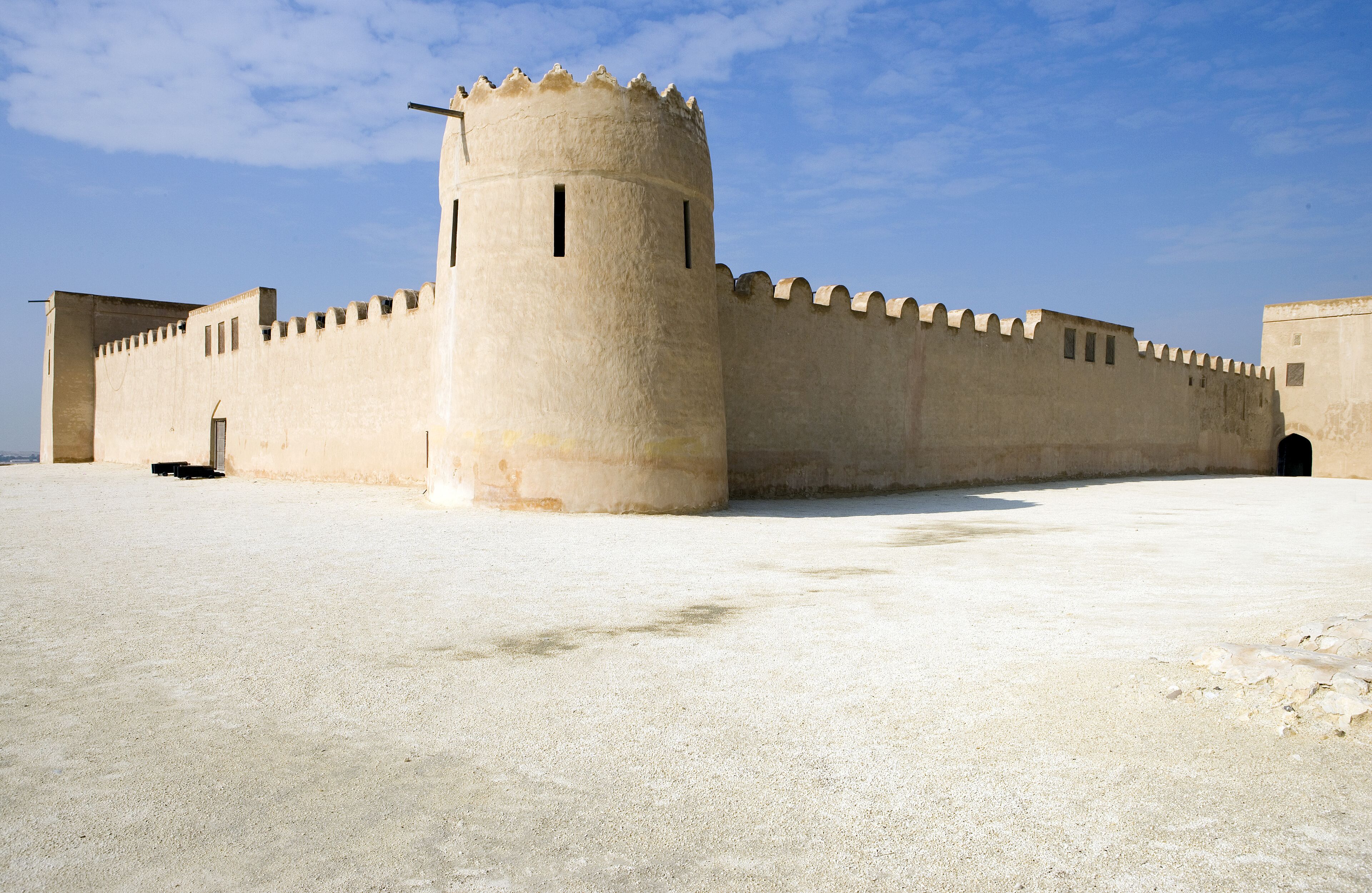A large, beige fortress with a round tower and crenellated walls.
