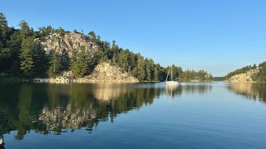 A calm lake with a sailboat, surrounded by dense forests and rocky cliffs.