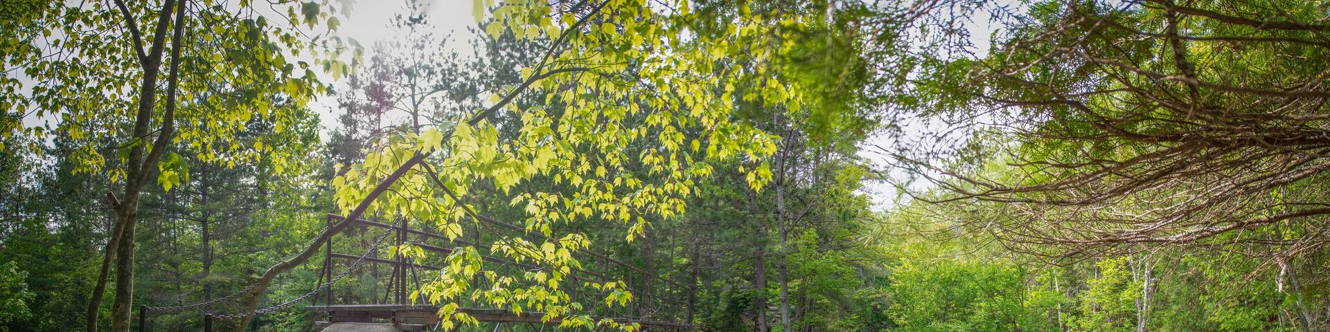The blurred water of Duchesnay Falls flows down a river, under a stone footbridge through a forest in North Bay, Ontario during sunset.