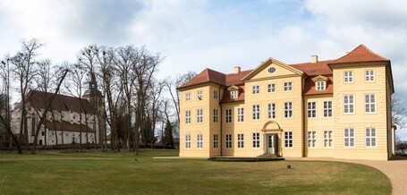 Ein großes, gelbes Gebäude mit rotem Dach, umgeben von einer gepflegten Rasenfläche und kahlen Bäumen.