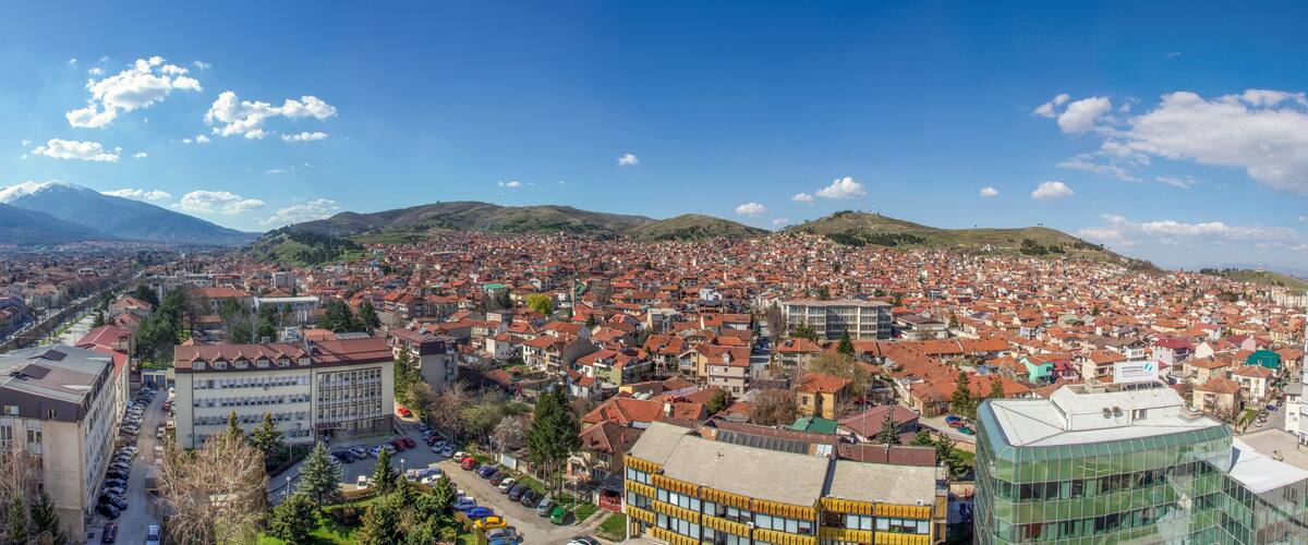 A cityscape with a mountain in the background, red-roofed buildings, and a mix of modern and traditional architecture.