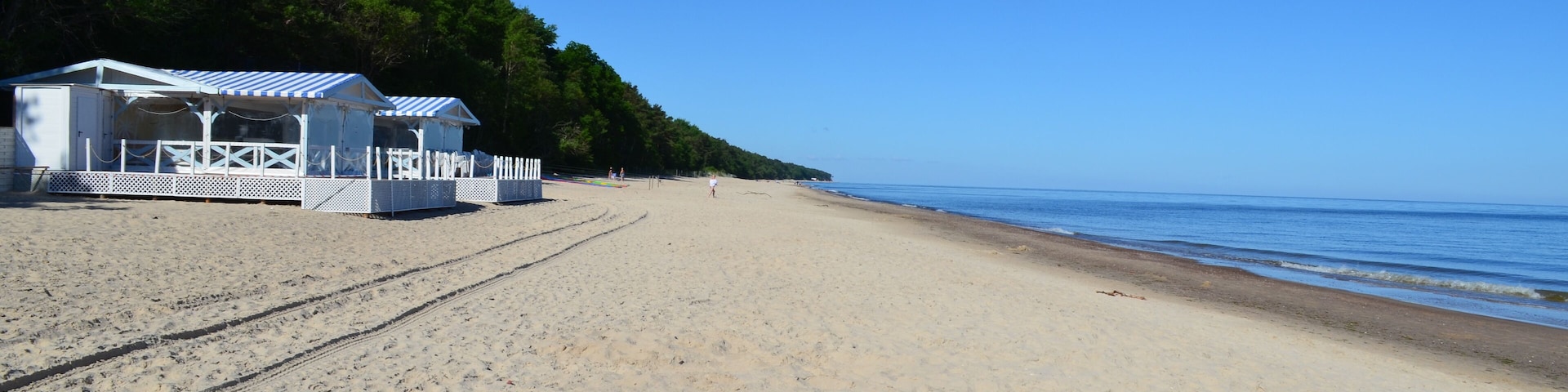 A sandy beach with a white building and a forested hill in the background.