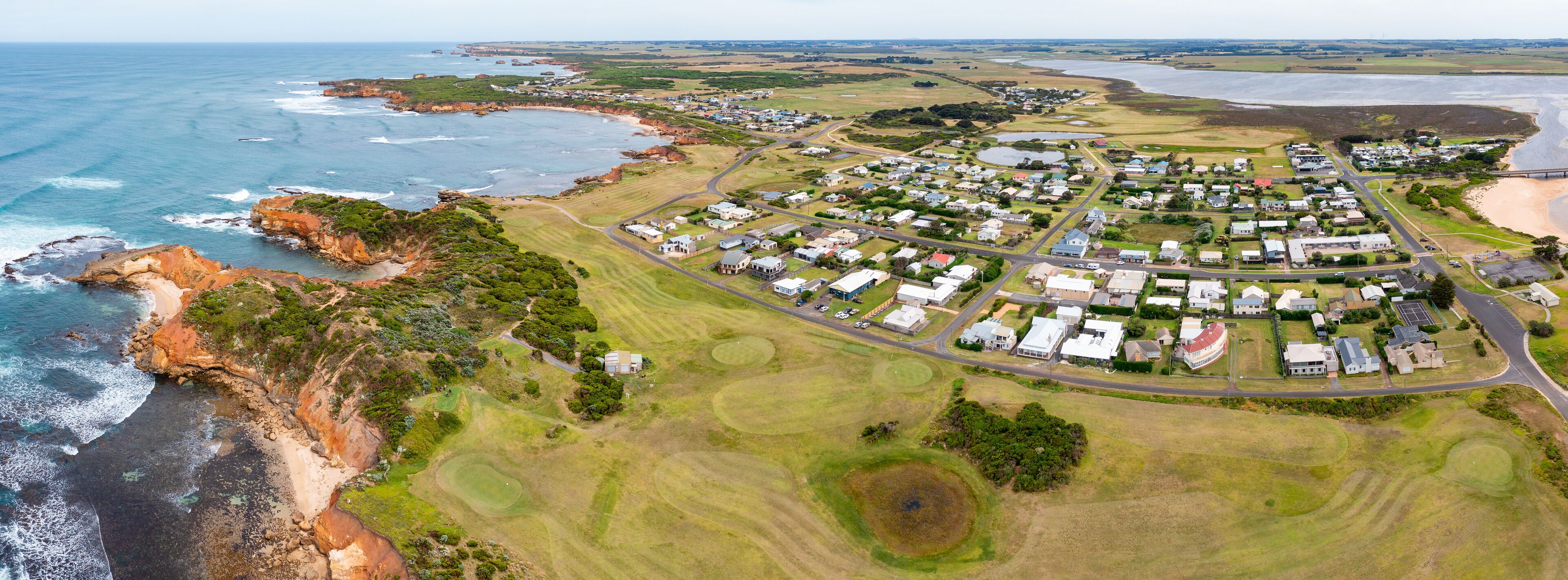 Aerial panorama of a small coastal town and golf course perched above a rugged coastline