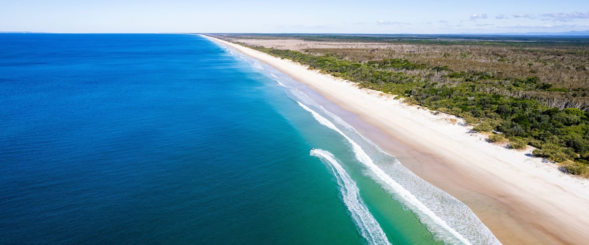 An aerial view of a beach with clear blue waters and a sandy shore.