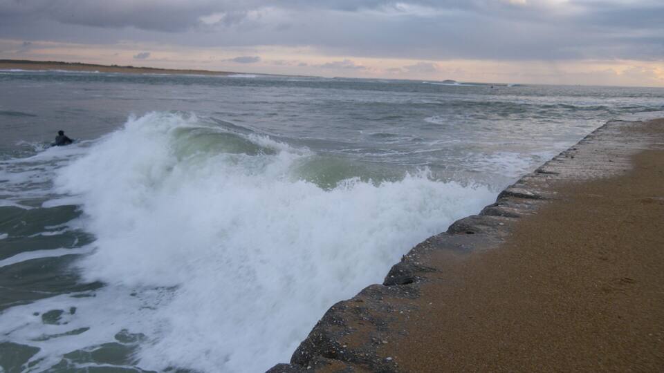 A beach with waves crashing onto the shore and a cloudy sky.