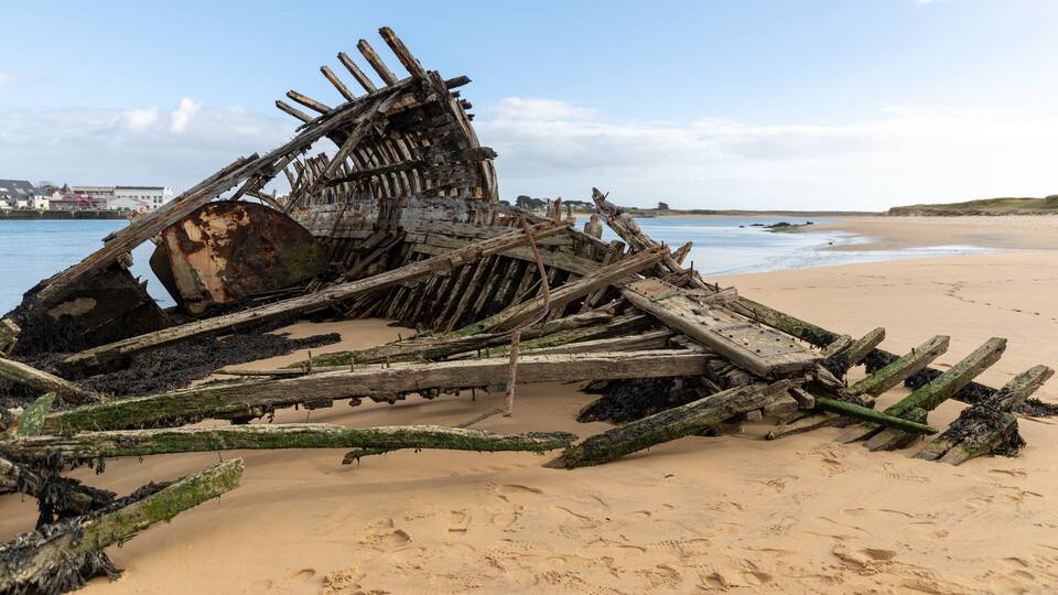 A sunken shipwreck on a sandy beach with a clear sky.
