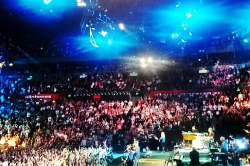 Un concert avec un public nombreux, des jeux de lumière sur scène et une foule de spectateurs.